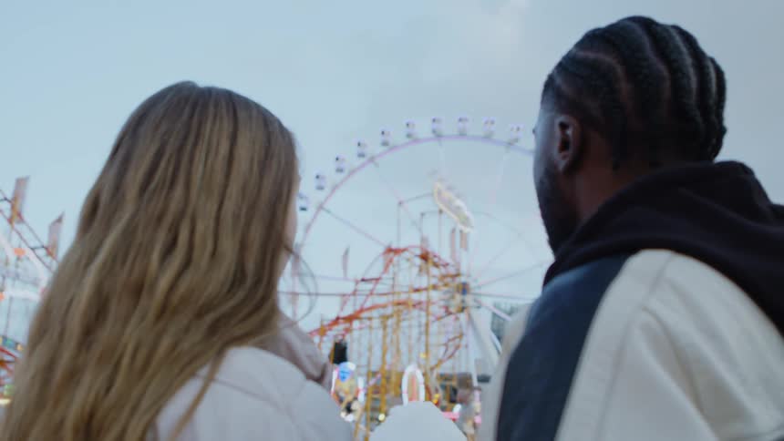 Young couple looking at the ferris wheel on an amusement park at evening