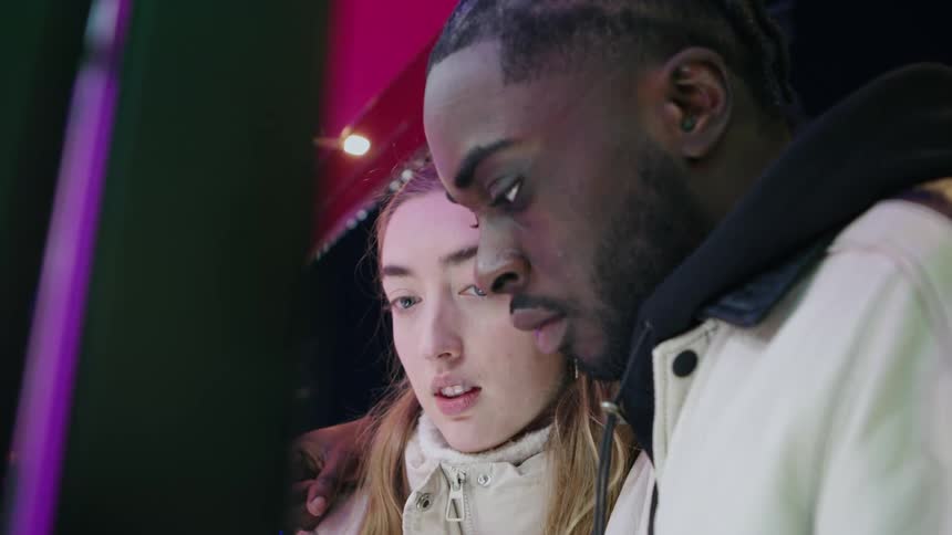 Man and woman on a date at nighttime looking at something in a shop window and talking