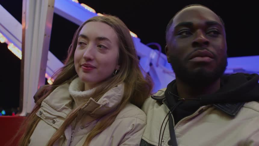 A man puts his arm around his girlfriend while riding a ferris wheel