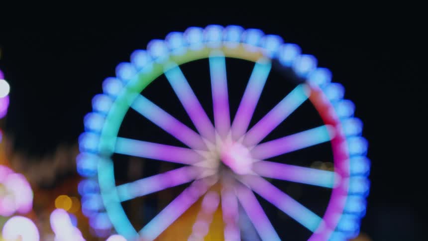 Bright colorful wheel with spokes slowly rotates against night sky