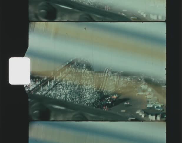 The camera captures a large white roller coaster that has many cars parked nearby