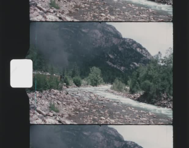 A stream runs down a forested mountain under a cloudy sky