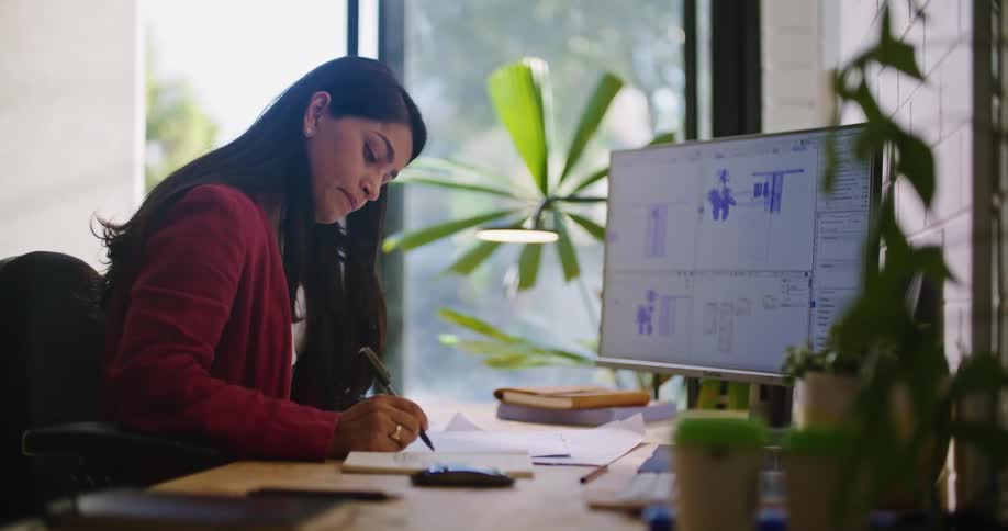 A woman takes notes while sitting at her desk