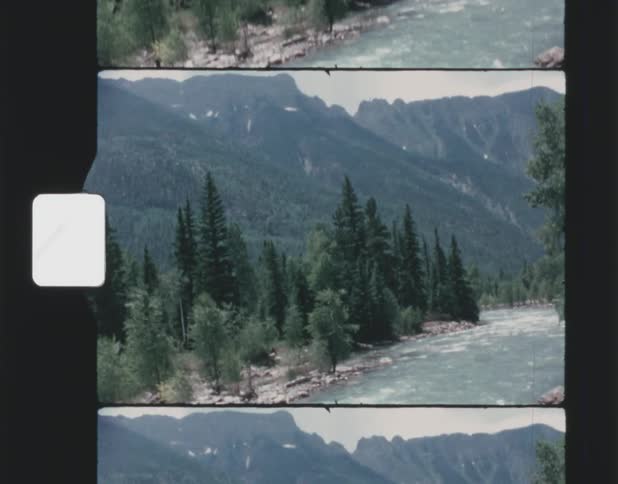 Old film footage of a river flowing through a forest with a mountain range in the background