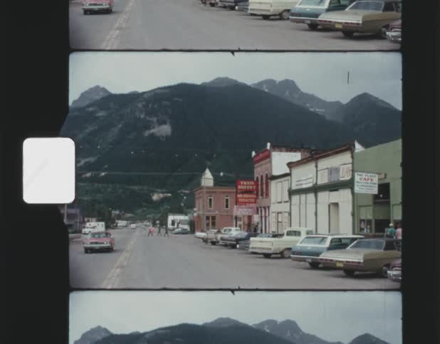 Vehicles line the street of a small town below a mountain