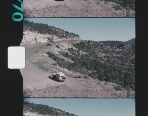 A wide view of a car parked at the end of a road with trees along the mountainside