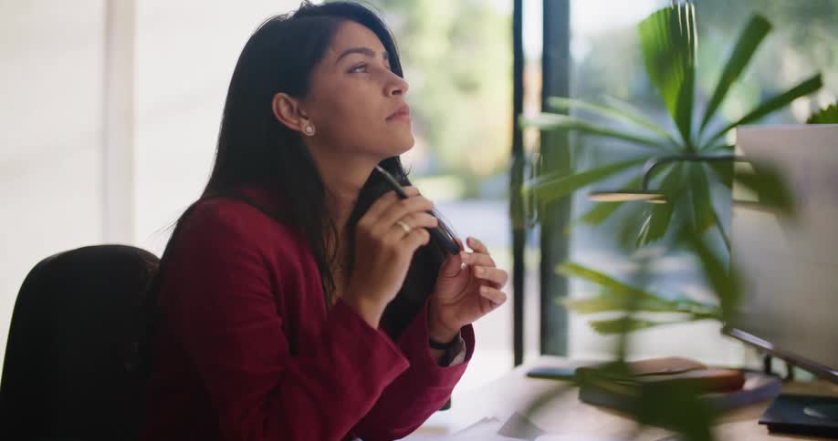 Businesswoman with red blazer sits at desk and writes down in notebook thinking of ideas