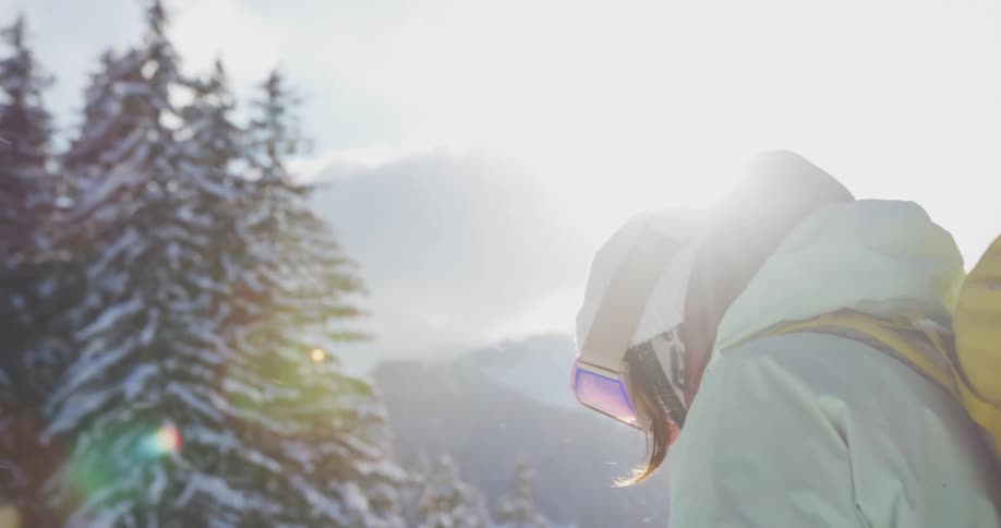 A woman wearing a winter jacket and backpack stands and looks down on an unseen mountain or other high point