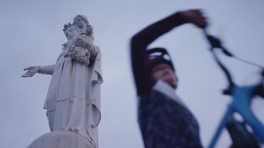 Male cyclist with helmet and jersey shirt stands next to monumento a la virgen del socavon