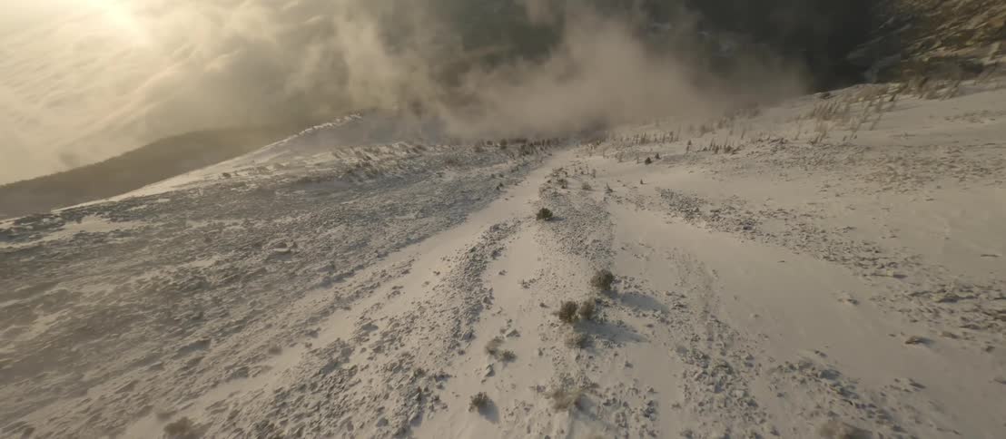 The camera swoops down and flies low above a snow covered mountain slope