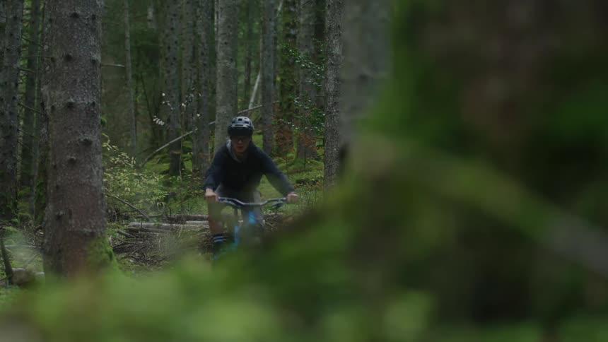 Cyclist with helmet jacket pants and glasses rides mountain bicycle in green woods