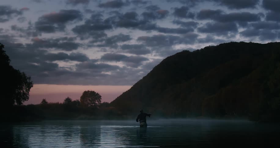 A person wading and fishing in a lake at sunset