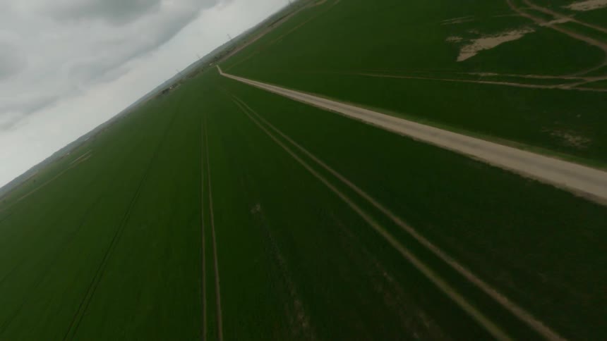 Wind turbines rotate under an overcast sky in field across road from crop fields