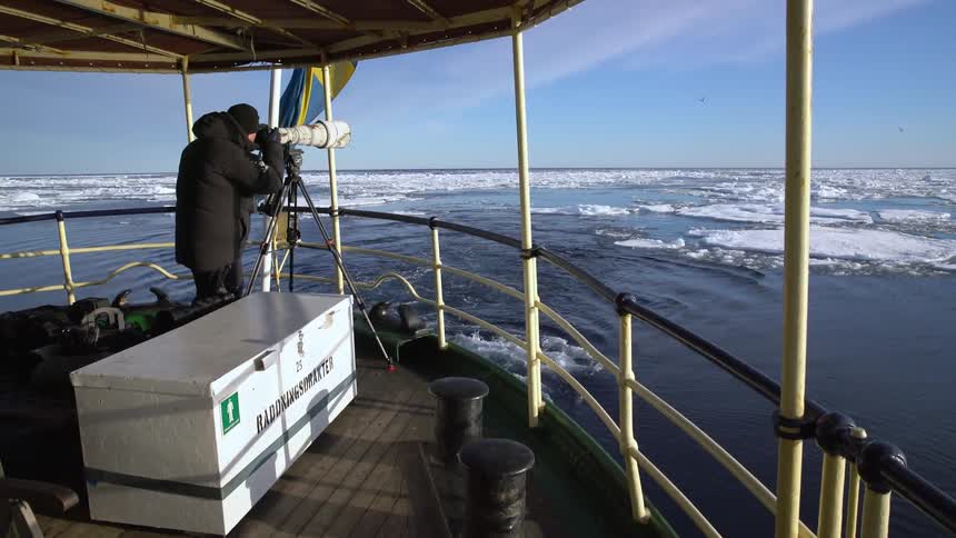 A photographer focuses a large lens off the back of a moving boat