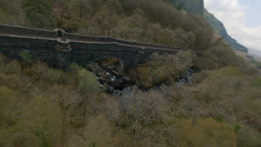 An aerial view of a bridge over a stream in a mountain setting