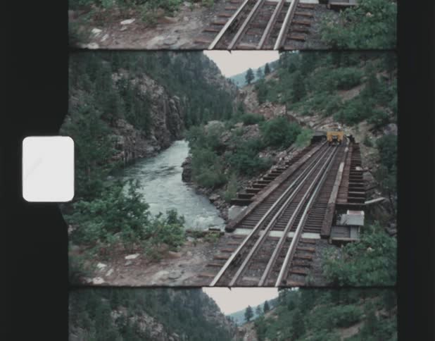 A train travels through a mountain river valley and over a bridge