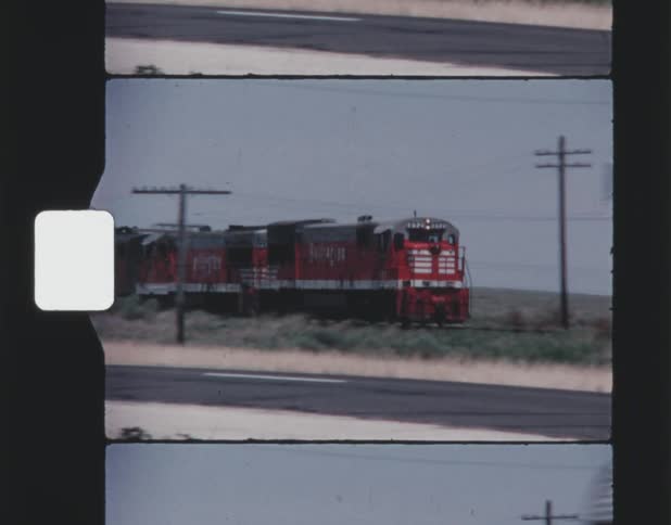 Red train runs along railway tracks next to highway