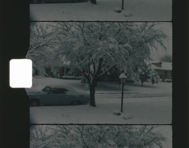 The view is of a neighborhood and it is snowing outside