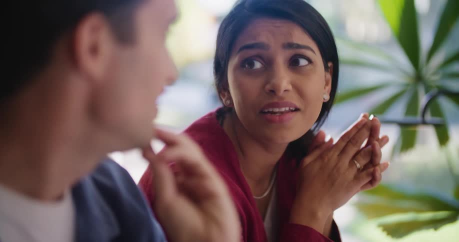 Woman with red shirt and dark hair looks at computer and talks with man with mustache and blue shirt at the office