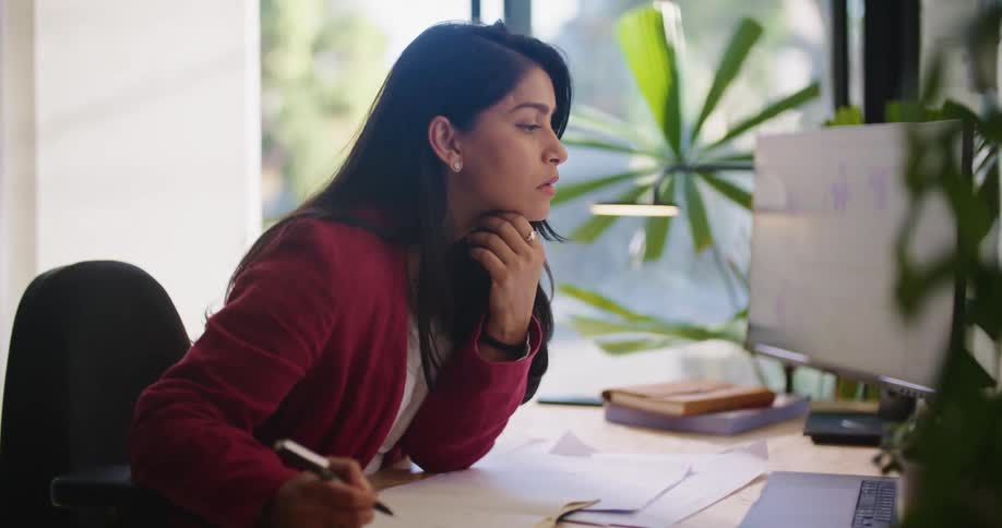 A woman takes notes while looking at her computer monitor