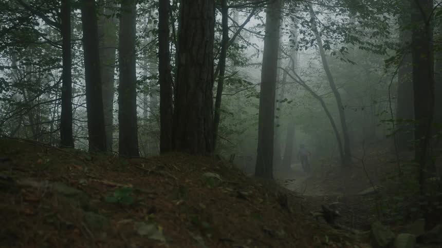 A teenage boy rides his bike fast on a trail in the smoke filled woods