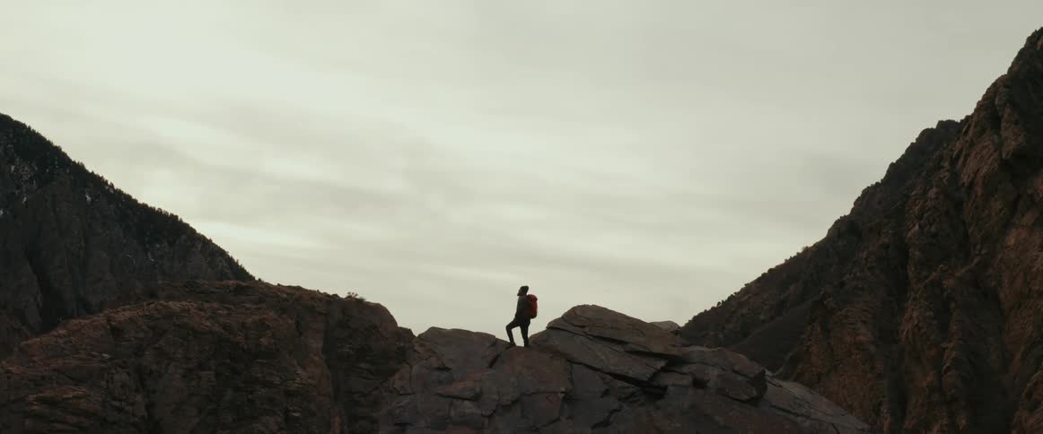 Mountaineer with backpack on rock against the cloudy sky