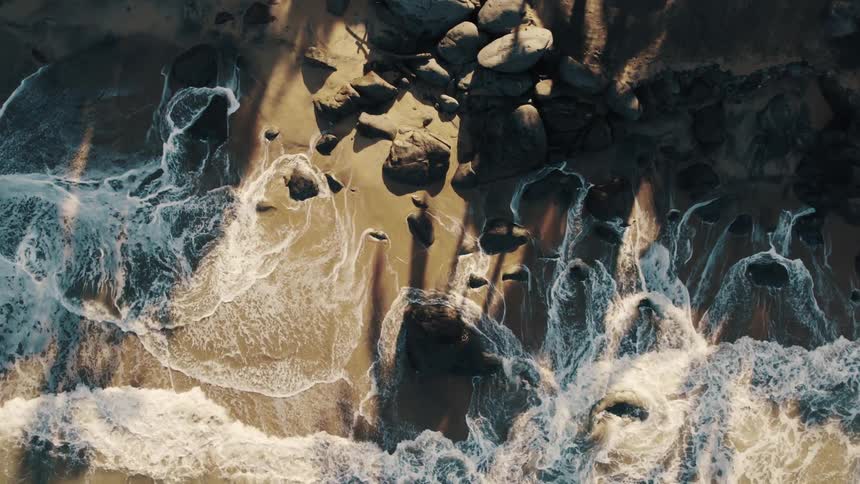 Ocean waves wash into a sandy beach littered with stones during the day