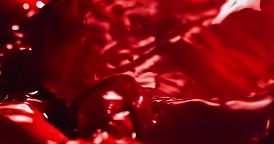 A close up of red liquid sloshing around creating splashes and bubbles