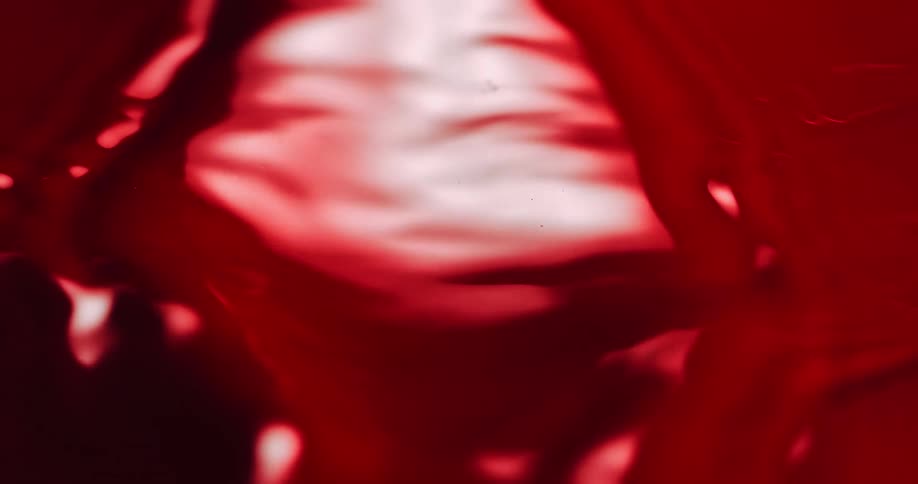 Ripples move across a shiny red liquid surface as it stretches and moves