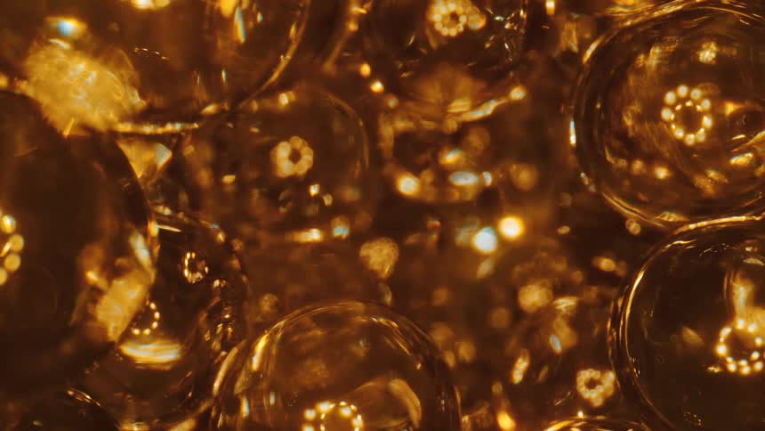 Clear spheres reflect rings of golden light as they fall and move