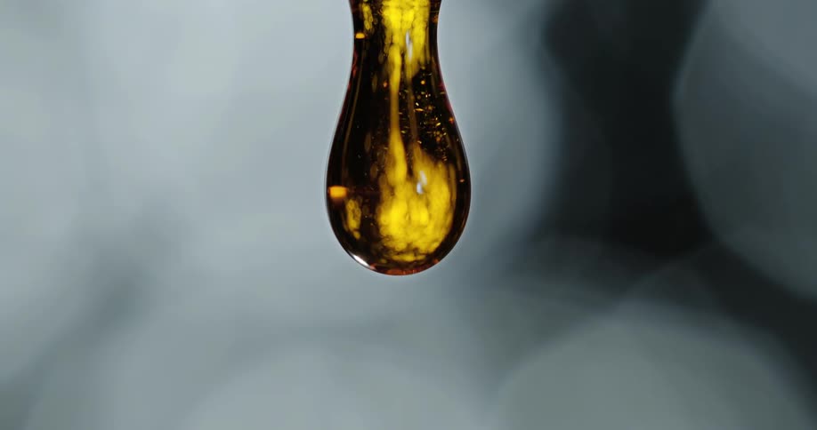 A close up of oil dripping down slowly and forming a droplet