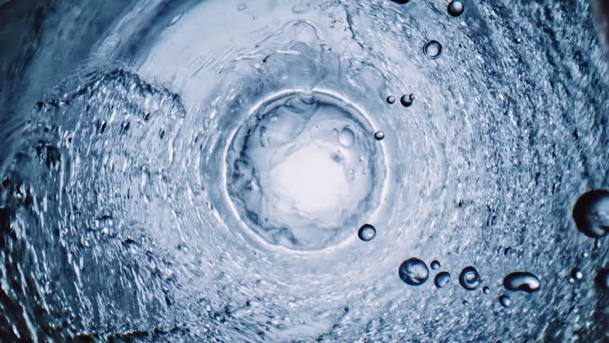 Water spins around the sides of a tunnel as droplets fall down toward the white center of the vortex