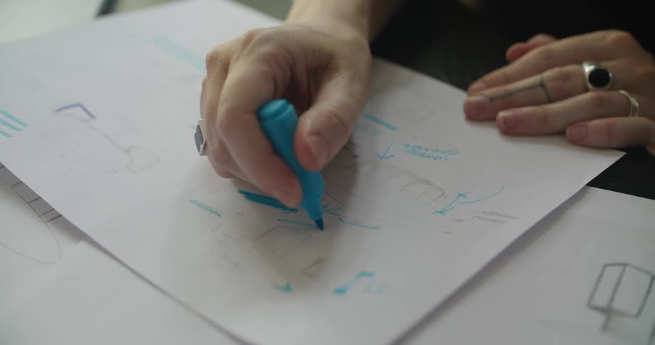 A woman uses a highlighter to outline a sketch on paper