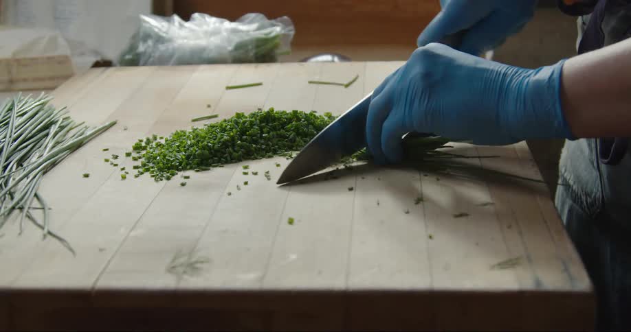 A woman is standing over a cutting board slicing herbs