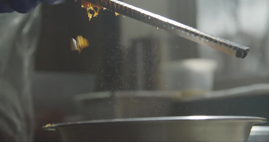 A cook is standing over a silver bowl grating orange peels