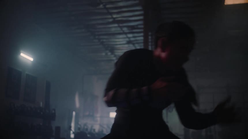 A woman practices kickboxing in a dim gym