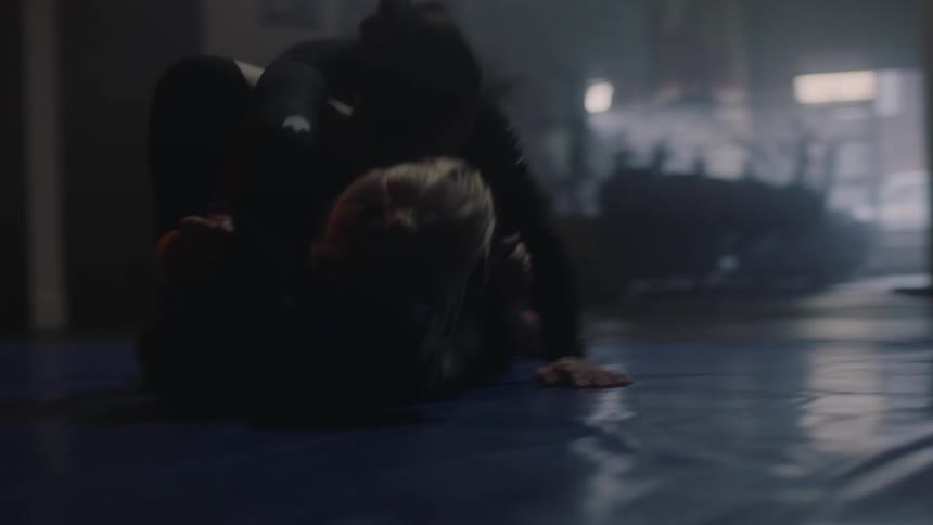 Two women grapple against each other on a mat inside of a gym