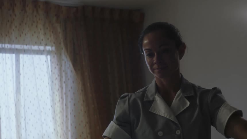 Cleaning lady makes bed in room