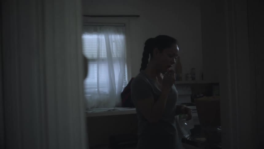 Woman with ponytail and gray t shirt stands in the kitchen