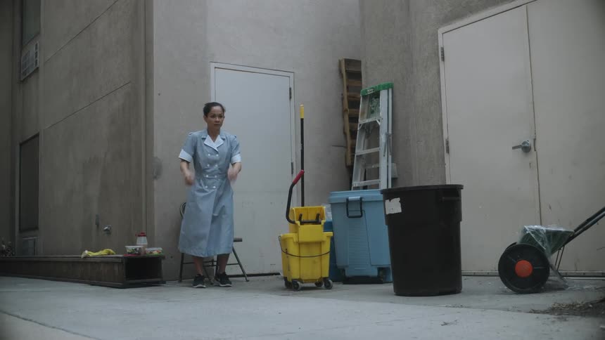 A housekeeper sitting in an alley finishing lunch stands and practices boxing motions