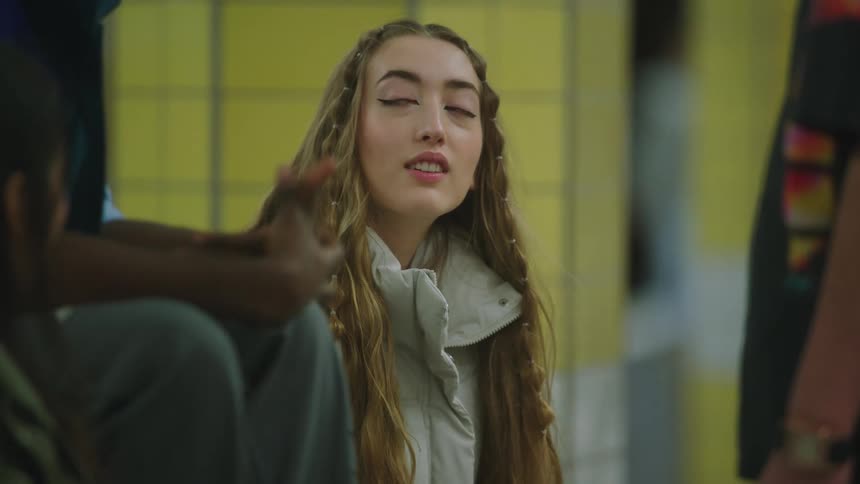 A teenage girl is sitting down talking to a guy sitting near her and another person is standing