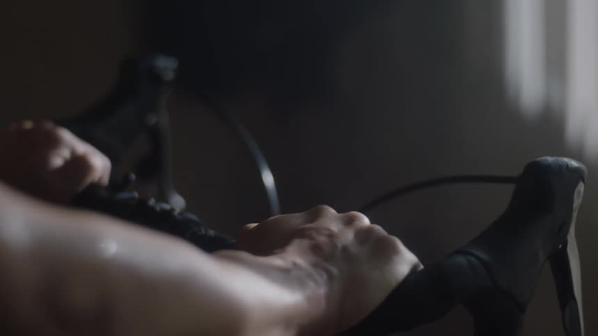 A woman pedals on a stationary bike while gripping the handles tightly