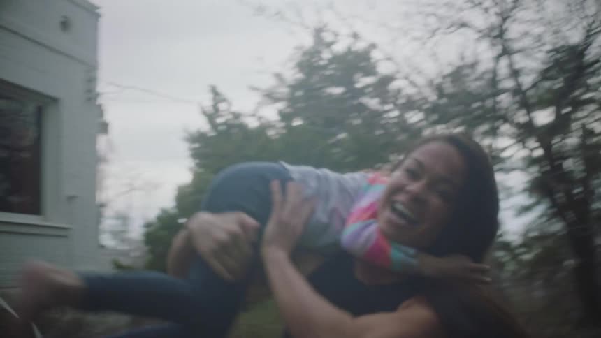 Mother plays with her daughter in house yard by picking up and spinning the child