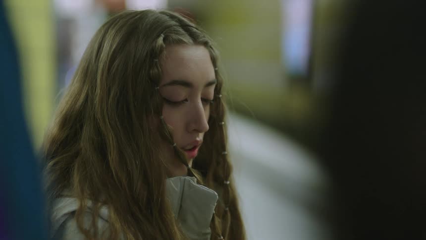 A teenage girl is sitting down as she takes off her headphones and looks around sad like she has been crying