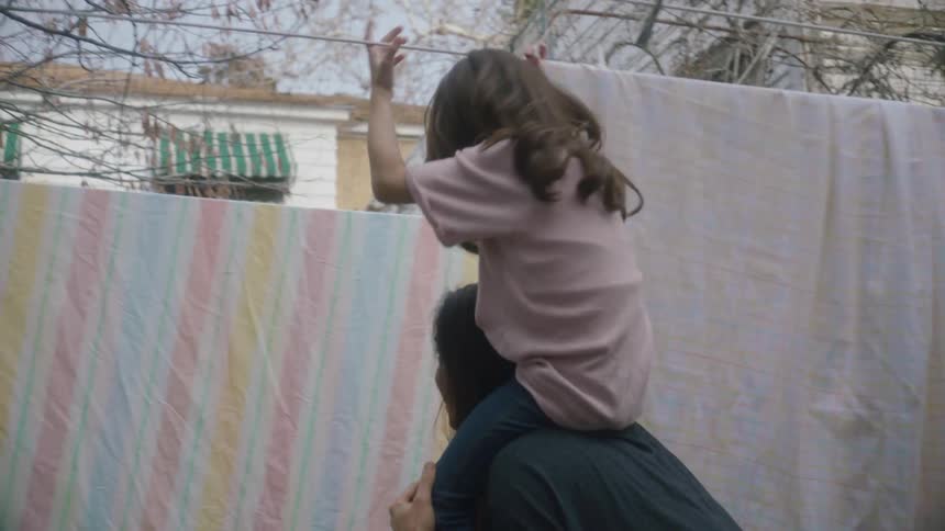 Mother carries daughter on her shoulders through clotheslines in the backyard