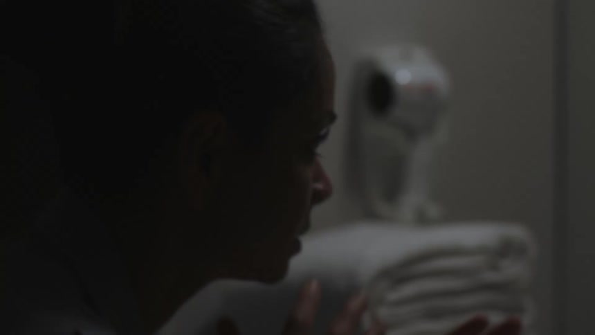 Woman wearing gray in bathroom poses while staring at her reflection