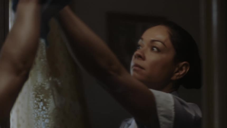 A housekeeper spraying and washing a mirror with her face reflects in it