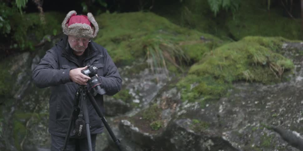 A man in a fur cap adjusts a camera