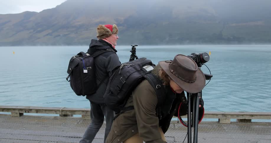 A man and woman walk towards the water and set up cameras