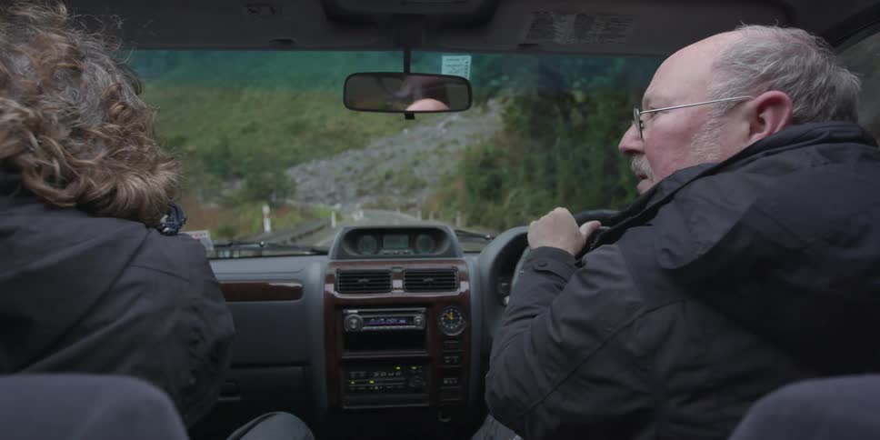 Two people are in a vehicle driving along a small road